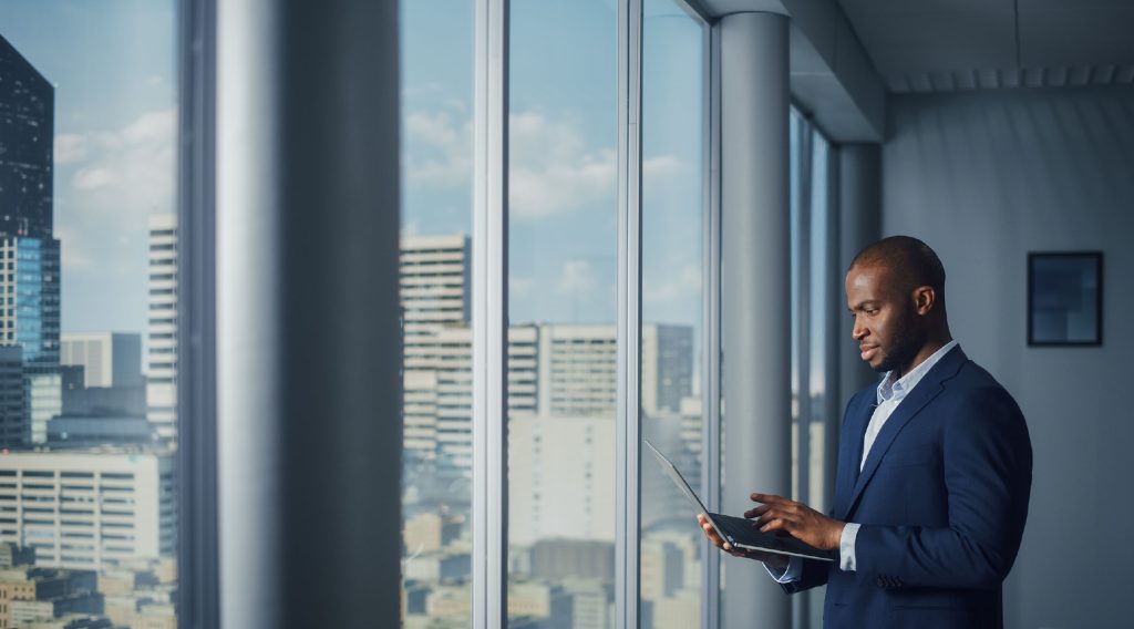Professional man in a suit standing near large windows in an office building.