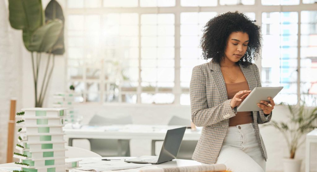 Professional woman standing in a bright, modern office space, using a tablet.
