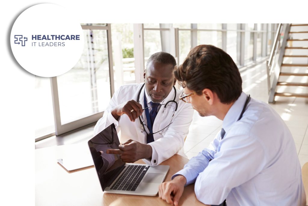 Two healthcare professionals reviewing information on a laptop in a bright medical office, with the Healthcare IT Leaders logo in the corner.