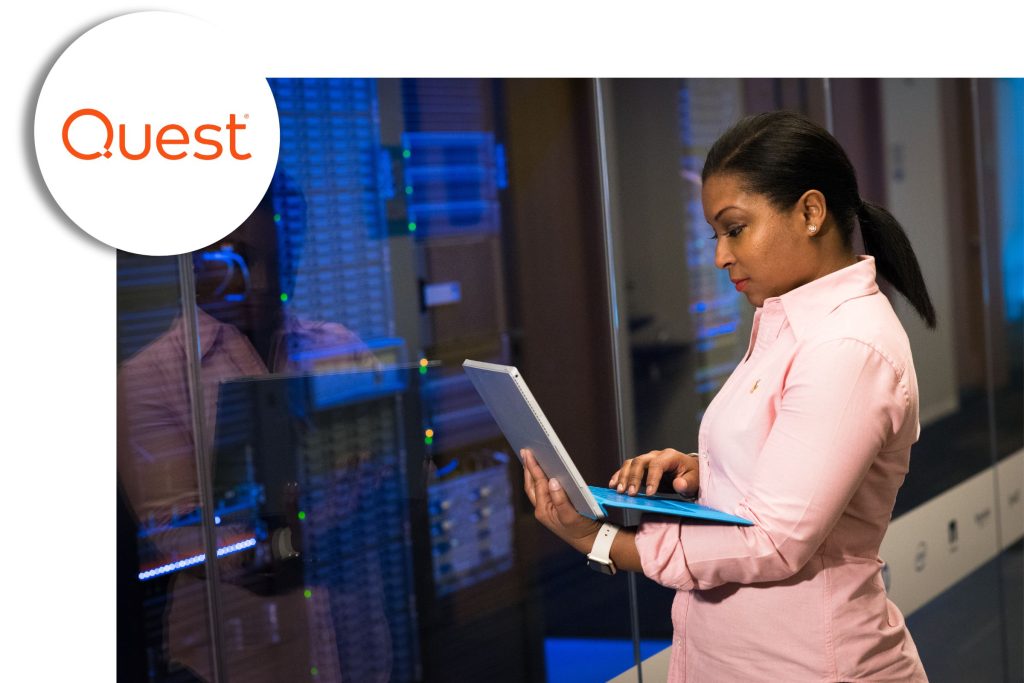 IT professional working on a laptop while standing beside illuminated server racks, with the Quest logo shown in the corner.
