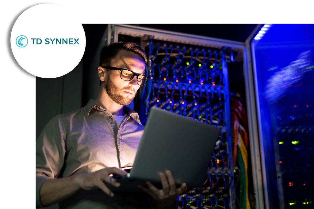 IT technician using a laptop while standing in front of illuminated server racks, with the TD SYNNEX logo shown in the corner.