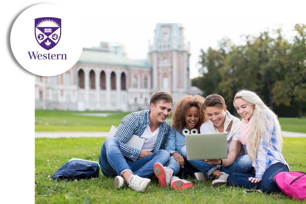 Group of university students sitting on the grass, smiling as they look at a laptop together, with the Western University logo in the corner.