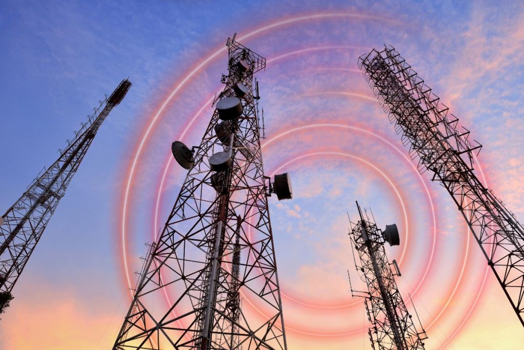 Multiple telecom towers rise against a colorful sunset sky.