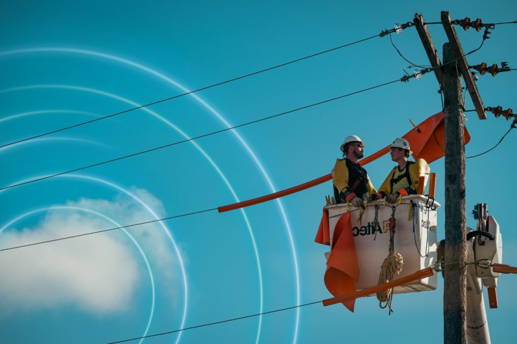 Two utility workers in safety gear performing maintenance on overhead power lines.