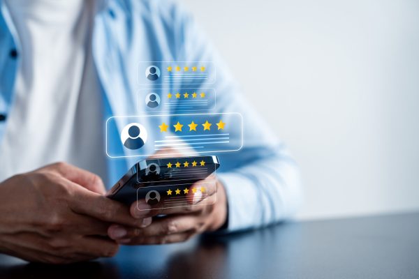 Person holding a smartphone with floating digital five-star rating icons representing online reviews and customer feedback.