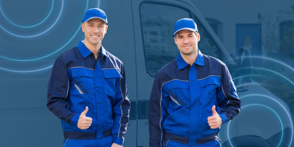 Two field technicians in blue uniforms standing in front of a service van.