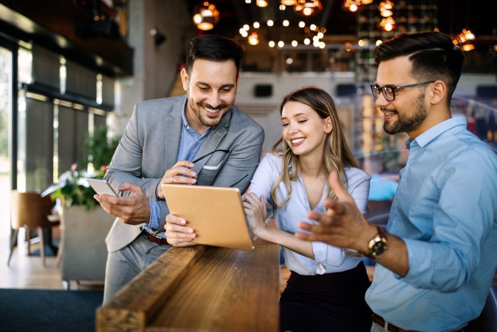 Three colleagues collaborating and reviewing information on a tablet in a modern workspace.